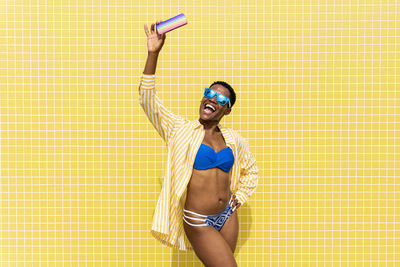 Cheerful woman in bikini taking selfie through smart phone