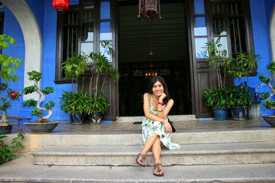 Portrait of smiling young woman sitting on steps with house in background