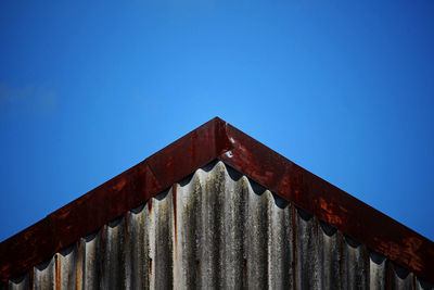 Low angle view of rusty metallic structure against blue sky