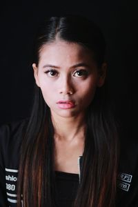 Close-up portrait of young woman against black background