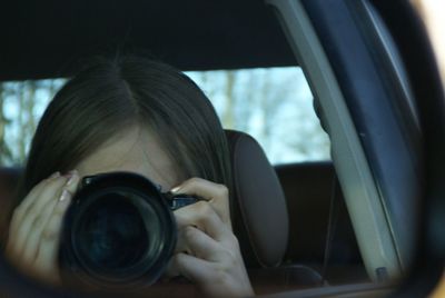 Reflection of girl photographing with camera on side-view mirror of car