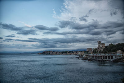 View of buildings by sea against cloudy sky