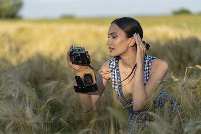 Young woman photographing while standing on field