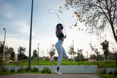 Woman exercising with jump rope against sky