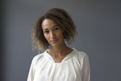 Portrait of young woman wearing white blouse against grey background