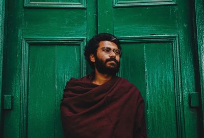 Man wrapped in shawl standing by wooden door