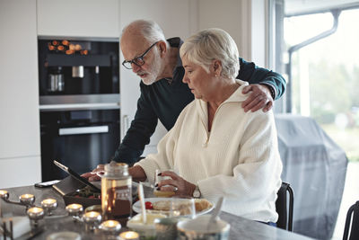 Senior couple looking at digital tablet while sitting by dining table in living room