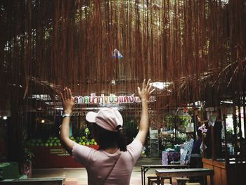 Rear view of young woman with arms raised standing in cafe