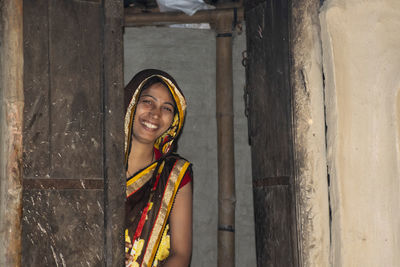 Portrait of a smiling young woman standing at door of the house