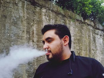 Man exhaling smoke while standing against wall