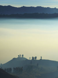 Silhouette people standing on mountain peak during foggy weather