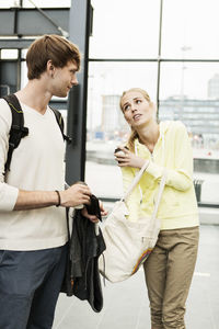 Man looking at friend searching something in bag at railroad station