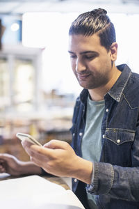 Smiling man using smart phone while sitting in supermarket