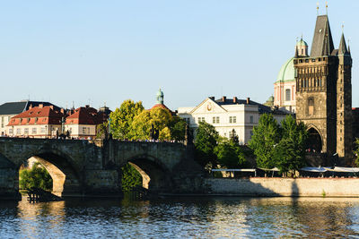 Arch bridge over river by buildings against clear sky