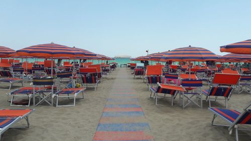 Empty chairs and tables at beach against clear sky