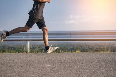 Low section of man running on shore against sky