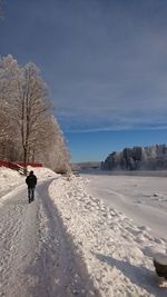 Rear view of man walking on snow covered road against sky