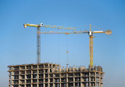 Low angle view of crane by building against clear blue sky