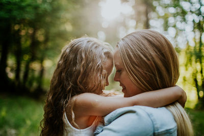 Mom and young daughter hugging smiling in afternoon sun