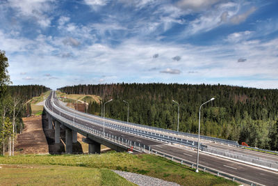 Bridge over road amidst trees on field against sky