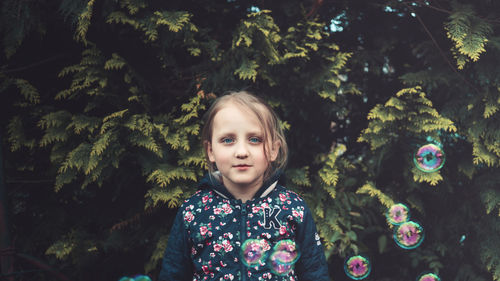 Portrait of girl standing amidst bubbles against plants