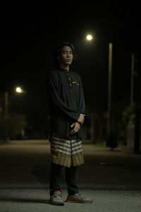 Young man looking away while standing on street at night