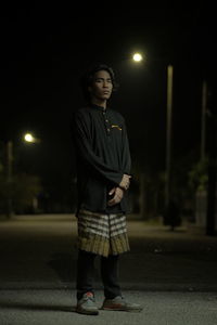 Young woman looking away while standing on street at night