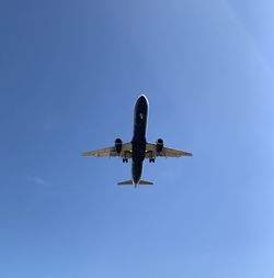 Low angle view of airplane flying against clear blue sky