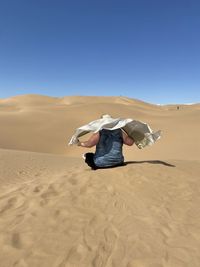 Rear view of man on sand in desert against clear blue sky
