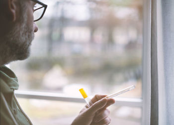 Close-up of man holding thermometer by window