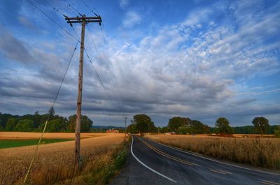 Empty road amidst landscape against cloudy sky