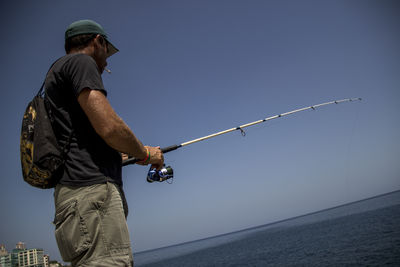 Low angle view of man fishing by sea against clear sky