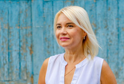 Portrait of smiling well-groomed middle-aged woman. blonde. bright makeup. blurred blue background