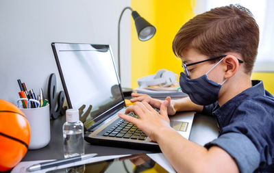 Boy wearing mask studying with laptop at home