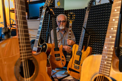 Middle-aged professional guitarist posing in his home recording studio amidst his guitar collection
