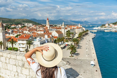 Rear view of woman standing on city walls looking at idyllic seaside town of trogir, croatia