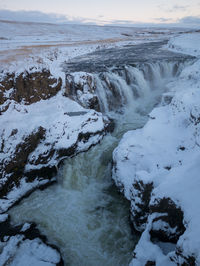 Scenic view of stream on snowcapped mountain against sky