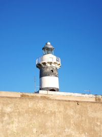 Low angle view of lighthouse against building against clear blue sky