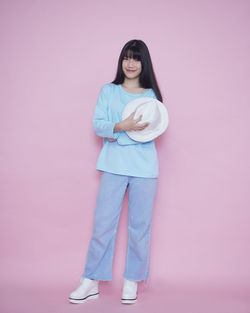 Portrait of young woman standing against pink background