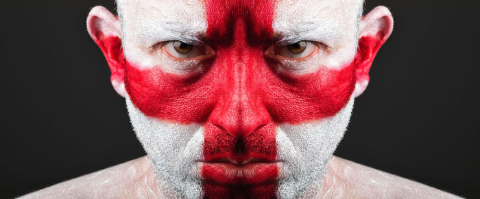 Close-up portrait of serious man with english flag body paint against black background