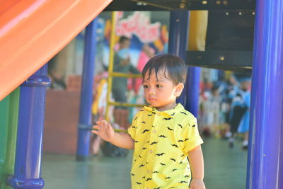 Cute boy looking away while standing by slide in playground