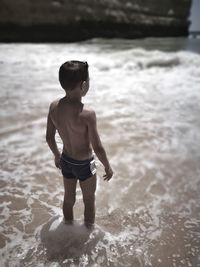 High angle view of shirtless boy standing in sea