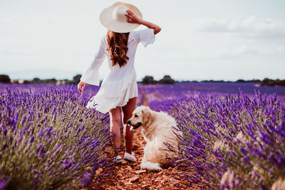 Rear view of woman with dog by flowering plants against sky