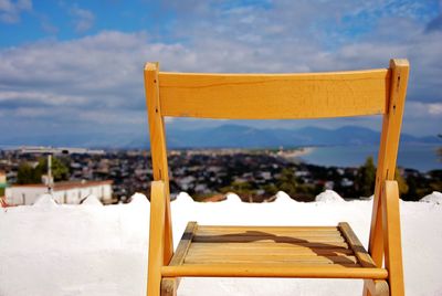 Chair on snow covered land against sky