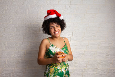 Happy woman holding camera while standing against wall