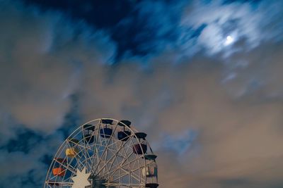 Low angle view of ferris wheel against cloudy sky at night