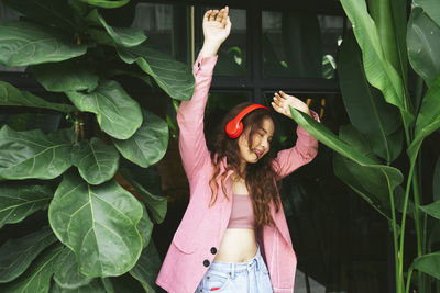 Young woman listening music while standing against window