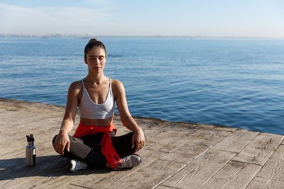 Young woman sitting on shore against sky