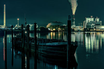 Illuminated buildings by river against sky at night