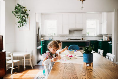 Two young kids doing arts and crafts in modern dining room.